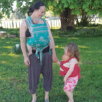 A mother with a baby on her chest holding the hand of a toddler